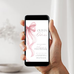 Peut inclure: Un smartphone affiche une invitation rose et blanche pour le premier anniversaire d'Olivia. L'invitation pr&eacute;sente un n&oelig;ud et des rubans &agrave; l'aquarelle. Le texte comprend la date, l'heure et le lieu.