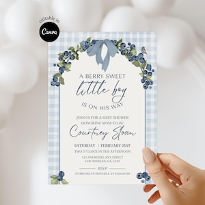 Puede incluir: Una invitación a un baby shower con un fondo de cuadros vichy azules y un diseño de arándanos y lazo. El texto dice "A Berry Sweet Little Boy is on His Way" e incluye detalles del evento, como la fecha, hora y lugar.