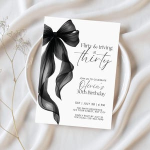 May include: A white invitation card with a black bow illustration. The text reads "Flirty & thriving at thirty" and invites guests to Olivia's 30th birthday. Includes date, time, location, and RSVP information.