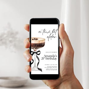 May include: A smartphone displays a birthday invitation with a watercolor illustration of a cocktail. The invitation text reads "a tini bit older" and "Amanda's 21st birthday". A black ribbon adorns the cocktail glass.