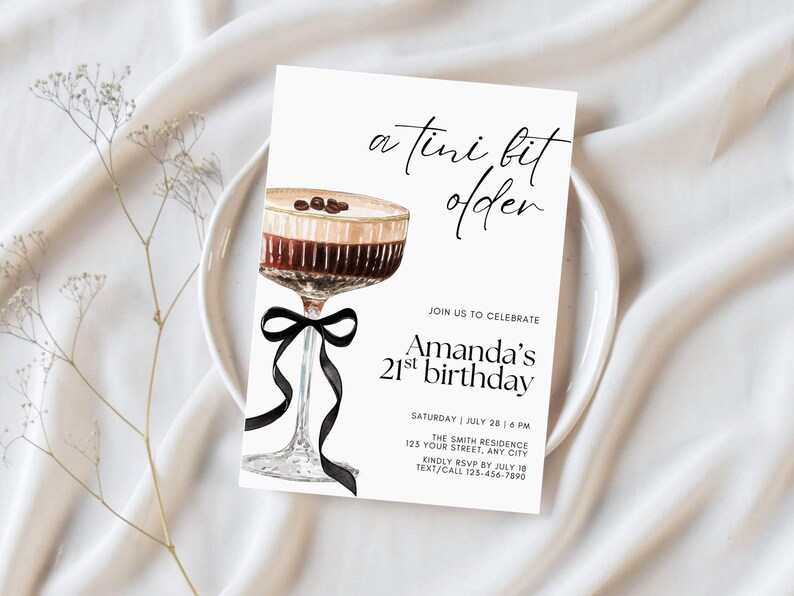 May include: A white invitation card with the text "a tini bit older" and "Amanda's 21st birthday". The card features a watercolor illustration of a cocktail with coffee beans and a black ribbon. The invitation is on a white plate.