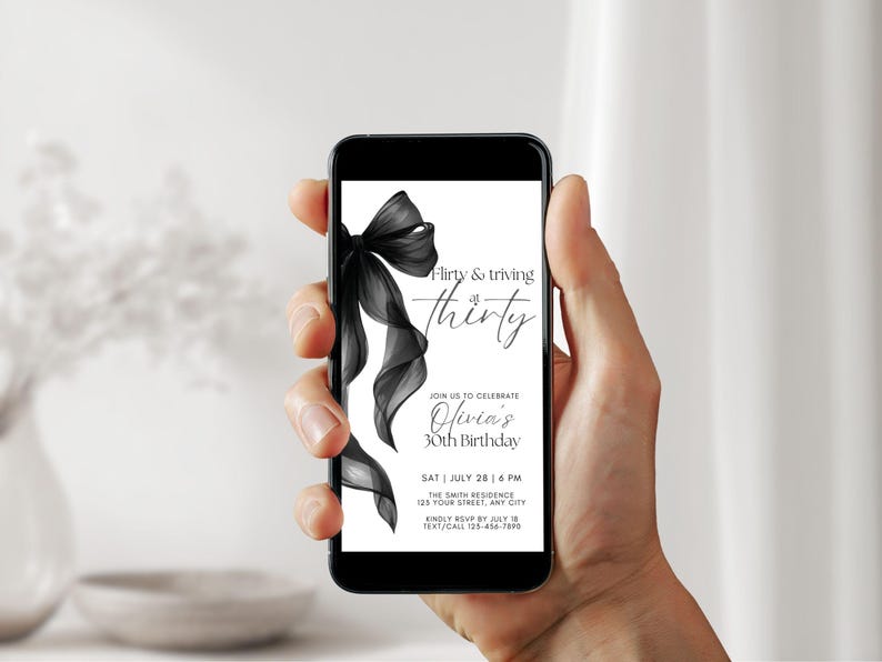 May include: A smartphone displays a black and white birthday invitation. The invitation features a black bow and the text "Flirty & thriving at thirty." Details include the date, time, location, and RSVP information for Olivia's 30th birthday.