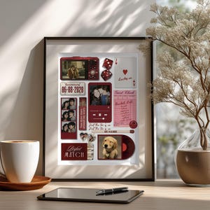 May include: A framed collage featuring photos, a red camera, dice, and a vinyl record. The collage includes the text "Anniversary 06-08-2020" and "Perfect Match". A cup of coffee and a tablet with a pen are on the table.