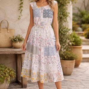 May include: A sleeveless patchwork midi dress with a square neckline. The dress features a mix of floral and geometric patterns in pastel colors. The model is wearing brown sandals. The background includes greenery and a stone patio.