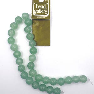 May include: A strand of round, light green beads attached to a rectangular cardboard header card labeled Bead Gallery with a length of 12 inches. The beads are smooth, opaque, and uniform in size, arranged in a single line on a clear string.