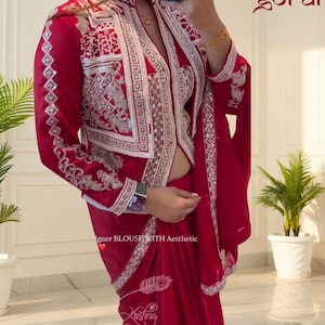 May include: A red ensemble featuring a jacket with intricate silver embroidery and a matching saree. The jacket has long sleeves and a detailed design around the edges. The text "goral" is visible in the upper right corner, and "igner BLOUSE WITH Aesthetic" is visible.