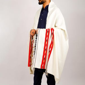 May include: Cream-colored shawl with red and black striped accents. The shawl has a fringed edge and is draped over the shoulders. The design features vertical stripes in red, black, and gold. The shawl is made of a soft, woven material.