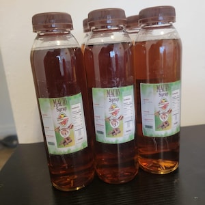 May include: Four clear plastic bottles filled with a brown liquid, each topped with a brown cap. The bottles have labels with the text "MAUBY Syrup" and a graphic. The bottles are arranged on a dark surface.