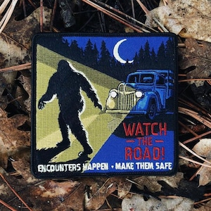 Puede incluir: Parche cuadrado con la silueta de un Bigfoot frente a un coche azul vintage. La escena nocturna incluye una luna creciente y un bosque. El texto dice "WATCH THE ROAD!" y "ENCOUNTERS HAPPEN • MAKE THEM SAFE."