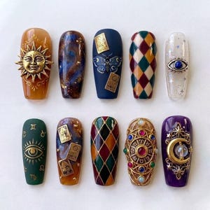 May include: A set of ten press-on nails featuring diverse designs including a gold sun charm, galaxy patterns, tarot cards, harlequin diamonds, an evil eye, zodiac symbols, a circular astrological wheel with colorful gems, and a gold moon charm.