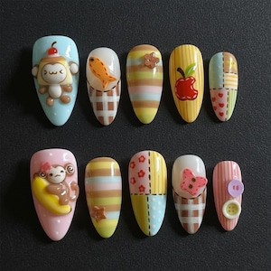 May include: A set of ten artificial nails with various designs. The nails feature cartoon monkeys, fish, apples, and patchwork patterns in pastel colors. Some nails have 3D embellishments like flowers and buttons.