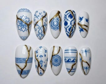 May include: A set of ten white artificial nails with blue floral and geometric designs, accented with gold crackle lines. The nail shapes are oval and feature various patterns, including flowers, circles, and waves.