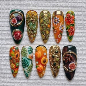 May include: A collection of ten long, almond-shaped, painted fingernails. Each nail features a unique design with 3D elements, including fruits like figs, pomegranates, and apricots, along with floral and leaf patterns. The color palette includes greens, oranges, and golds.