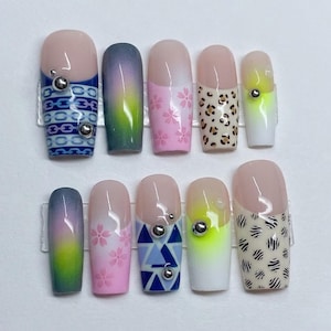 May include: A set of ten artificial nails with various designs. The nails feature a range of colors, including pink, blue, green, and white, with patterns like floral, animal print, and geometric shapes. Some nails have silver embellishments.