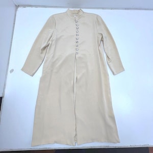 May include: A long, beige coat with a high collar and long sleeves. The coat has small, decorative buttons down the front. The fabric has a subtle sheen, suggesting a satin or silk-like material. The coat is a neutral colour, suitable for various outfits.