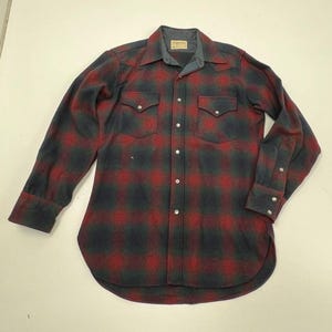 May include: A long-sleeved, button-down shirt in a red and navy plaid pattern. The shirt has two chest pockets, a gray collar, and buttoned cuffs. The shirt is made of a thick, warm material.