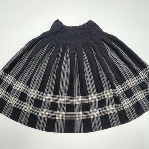 May include: A black pleated skirt with a white and black plaid pattern. The skirt has vertical stripes and a plaid design at the bottom. The skirt is made of a soft material and is suitable for casual wear.