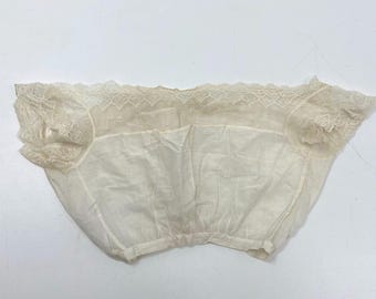 Puede incluir: Prenda interior vintage de color crema con delicados adornos de encaje a lo largo del escote y mangas cortas. La tela parece ser un material ligero y semitransparente, fruncido en la cintura. La prenda tiene un aspecto ligeramente envejecido.