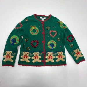 May include: Green Christmas sweater with red trim and buttons. The sweater features embroidered teddy bears, wreaths, hearts, and snowflakes. The sleeves and bottom hem have a scalloped edge.