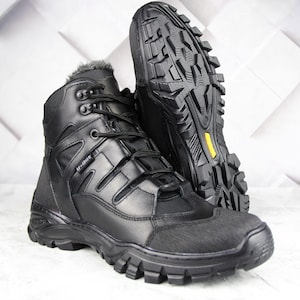 Puede incluir: Botas negras de cuero y tela con suela robusta y texturizada. Las botas tienen un diseño con cordones, un cuello acolchado y una puntera reforzada. La suela es gruesa y presenta un acento amarillo. Botas diseñadas para actividades al aire libre.