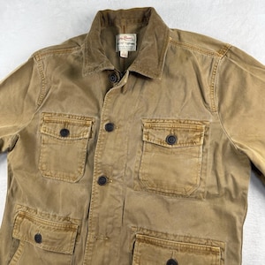 May include: A tan utility jacket featuring a corduroy collar, a button-front closure, and four front pockets with buttoned flaps. The interior label reads Lucky Brand, Los Angeles, California, and the size is marked as L.