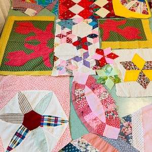 May include: A collection of assorted fabric quilt blocks featuring various geometric shapes, floral patterns, and solid colors including red, yellow, green, pink, and blue. The pieces display diverse stitching techniques, including star, fan, and hexagon motifs, arranged in a scattered layout.