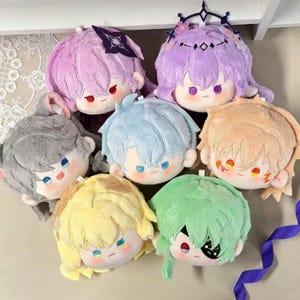 May include: Seven plush dolls in various colours, including pink, purple, grey, blue, yellow, green, and tan. Each doll has a different hairstyle and embroidered facial features. The dolls are designed in a cartoon style.