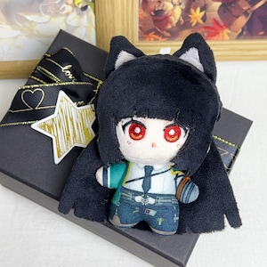 May include: A plush doll with black hair, red eyes, and cat ears. The doll is wearing a white shirt, blue jeans, and a teal backpack. It is sitting on a black gift box with a gold star and ribbon.