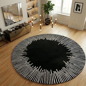 May include: A large, round black rug with a white, linear pattern around the edge. The rug is placed on a hardwood floor in a modern living space. The rug's design adds a striking contrast to the room's decor.