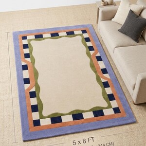 May include: Rectangular area rug with a light beige center and a border featuring a blue, orange, green, and checkered design. The rug measures 5 x 8 feet (approximately 152 x 244 cm).