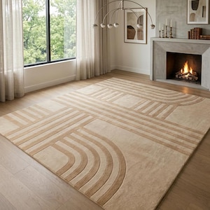 Puede incluir: Una alfombra rectangular grande con un patrón geométrico en tonos beige y marrón claro. La alfombra presenta líneas curvas y rectas, creando un diseño abstracto. Está colocada sobre un suelo de madera clara en una habitación luminosa.