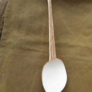 Peut inclure: Une cuillère en bois à long manche dotée d'un bol lisse de couleur crème et d'un manche fin et texturé avec des motifs de grain de bois naturel visibles. La cuillère présente une forme allongée et effilée avec une pointe à la base du bol.