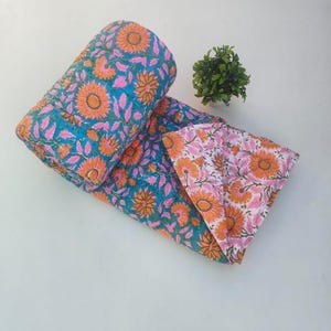 May include: A reversible quilted blanket featuring a vibrant floral pattern with orange sunflowers and pink leaves on a teal background, while the reverse side displays the same floral design in orange and pink on a white background.