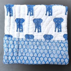 Könnte beinhalten: Eine gesteppte Decke mit weißem Hintergrund und einem sich wiederholenden Muster aus blauen Elefanten. Der untere Teil der Decke zeigt einen kontrastierenden Rand mit einem dichten, sich wiederholenden Muster aus blau-weißen Blättern in vertikaler Anordnung.