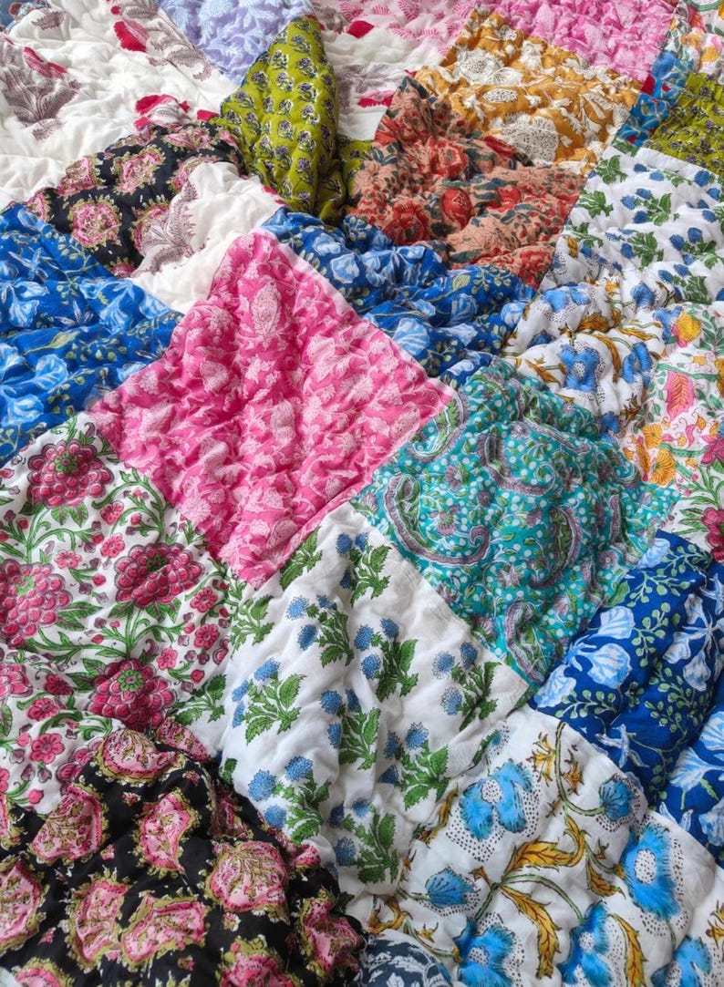 May include: A quilted blanket featuring a patchwork of square fabric panels in various colors including pink, blue, green, black, and yellow. Each square displays a distinct floral or paisley print pattern with a textured, puckered surface finish.