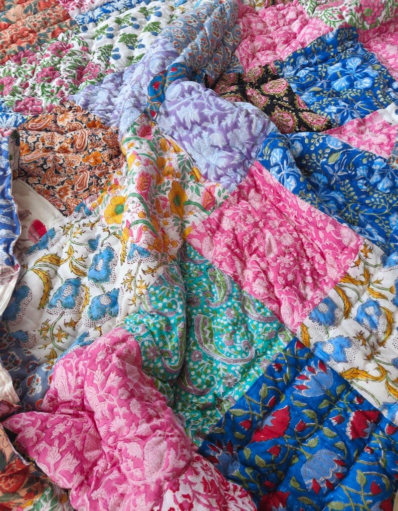 May include: A quilted patchwork blanket featuring a variety of floral and paisley block-printed patterns in vibrant colors including pink, blue, yellow, green, orange, and purple. The fabric has a textured, stitched finish throughout the surface.