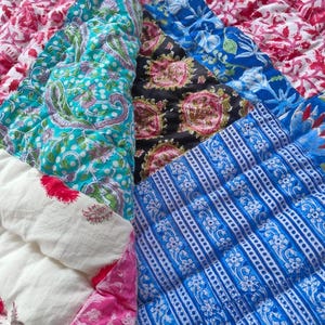 May include: A quilted textile featuring a patchwork of various printed fabrics in vibrant colors including magenta, turquoise, black, and royal blue. The patterns include floral motifs, paisley designs, and geometric stripes with visible stitching.