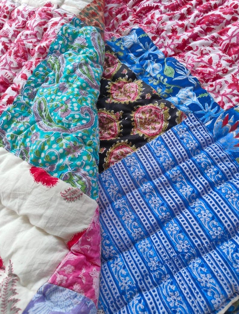 May include: A quilted textile featuring a patchwork of various printed fabrics in vibrant colors including magenta, turquoise, black, and royal blue. The patterns include floral motifs, paisley designs, and geometric stripes with visible stitching.