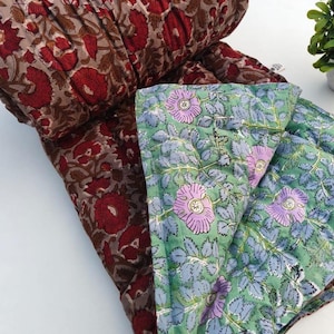 May include: A reversible quilted blanket featuring two distinct floral patterns. One side displays deep red flowers on a muted brown background, while the other side showcases light purple flowers with green leaves on a pale green background.