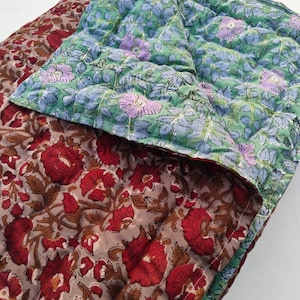 May include: A reversible quilted blanket featuring two distinct floral patterns. One side displays large red flowers with brown foliage on a light brown background, while the other side shows light purple flowers with green leaves on a light green background.
