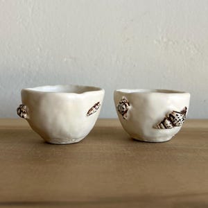 May include: A set of three ceramic mugs with a speckled, matte finish. The mugs are in shades of cream, light gray, and dark gray. Each mug has a simple, minimalist design, perfect for coffee or tea.