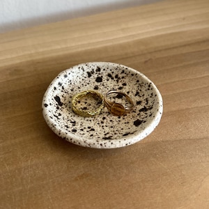 May include: A set of three ceramic mugs with a speckled, matte finish. The mugs are in shades of cream, light gray, and dark gray. Each mug has a simple, minimalist design, perfect for coffee or tea.