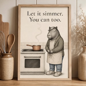 May include: A framed wall art print featuring a capybara wearing a sweater and apron, standing next to a stove with a steaming pot. The text reads, "Let it simmer. You can too." The illustration is rendered in a muted, sketch-like style.