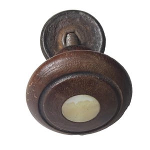 May include: A close-up of a vintage wooden cabinet knob. The knob is a dark brown color with a circular design and a light-colored center. The metal base is a dark, aged color.