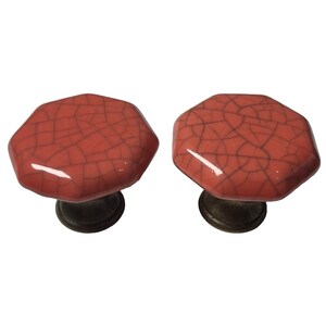 May include: Two coral-coloured octagonal cabinet knobs with a crackle glaze finish. They have a dark bronze base. These decorative knobs are suitable for furniture or cabinet upgrades.