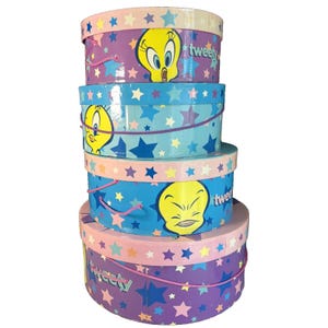May include: A stack of four round storage boxes featuring the cartoon character Tweety Bird. The boxes are decorated with stars and the word "tweety". The boxes are in shades of blue, purple, and pink.