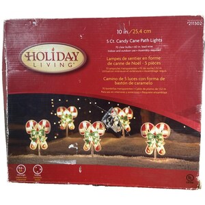 May include: A box of Holiday Living 5 Ct. Candy Cane Path Lights. The box is red with images of candy cane lights with green bows. The lights are 10 inches (25.4 cm) tall and have 70 clear bulbs. Indoor and outdoor use.