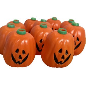 May include: A collection of orange, smiling jack-o'-lantern decorations with green stems. Each pumpkin has a carved face with triangular eyes and a curved mouth. The pumpkins are arranged closely together, creating a festive Halloween display.