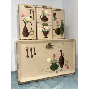 Peut inclure: Un ensemble de rangement de cuisine vintage en métal crème comprenant quatre boîtes et une boîte à pain. Chaque pièce est décorée d'illustrations peintes de compositions florales dans des vases, pichets et ustensiles de cuisine suspendus.