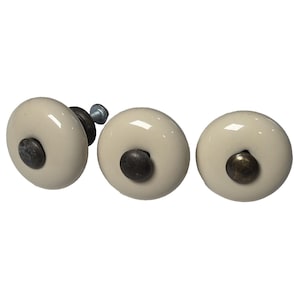 May include: Three off-white ceramic cabinet knobs with dark metal accents. The knobs are round with a slightly domed shape and a glossy finish. The hardware includes a screw for installation. Ideal for furniture or home decor projects.